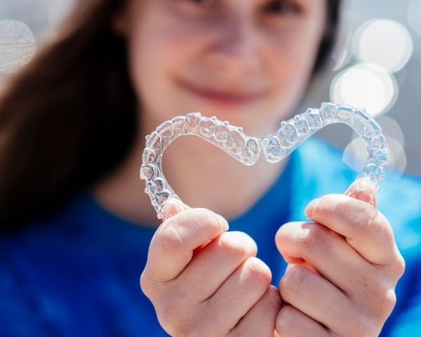 dental-care-smiling-beautiful-girl-holding-heartshaped-aligners-plastic-retainers-teeth-alignment_114354-6401